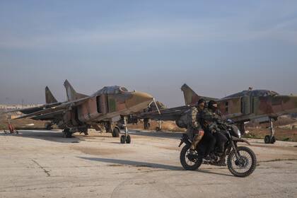 Combatientes opositores sirios a bordo de una motocicleta frente a aviones del ejército sirio en el aeropuerto militar de Al-Nayrab después de asumir el control de las instalaciones, el lunes 2 de diciembre de 2024, a las afueras de Alepo, Siria. (AP Foto/Omar Albam)