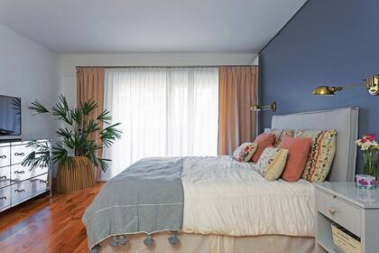 Cómoda revestida en espejos biselados, cama con respaldo en tussor (ambas de Olivia D), acolchado traído de un viaje, almohadones varios (Rapsodia Home) y, en el rincón, maceta (Sentido).