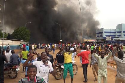 Con la sede del gobierno ardiendo de fondo, partidarios de los soldados amotinados se manifiestan en Niamey, Níger, el 27 de julio de 2023. (AP Foto/Fatahoulaye Hassane Midou)