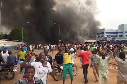 Con la sede del gobierno ardiendo de fondo, partidarios de los soldados amotinados se manifiestan en Niamey, Níger, el 27 de julio de 2023. (AP Foto/Fatahoulaye Hassane Midou)