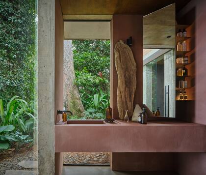 Con una ducha amplia y vista al mar, el baño se conecta tanto con la terraza de la pileta como con el sendero de acceso y el interior de la casa. Las superficies están terminadas en microcemento pigmentado.