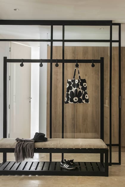 Con una fuerte carga geométrica y un sistema de colgado con roldanas, el mudroom es ideal para dejar bolsos y sandalias a la vuelta de la playa. El tapizado de la colchoneta, a tono con los muebles de guardado que deja ver el cerramiento transparente.