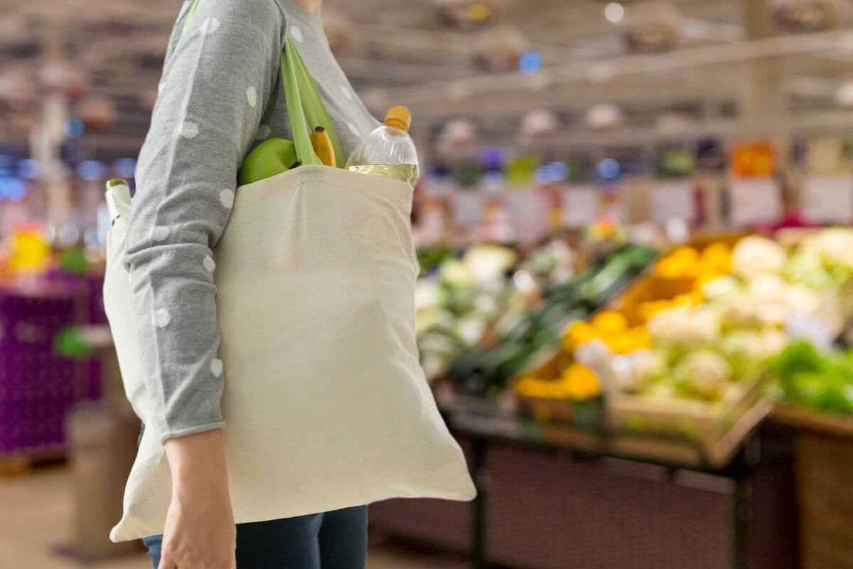 consumerism, eating and eco friendly concept - woman with white reusable canvas bag for food shopping over supermarket on background