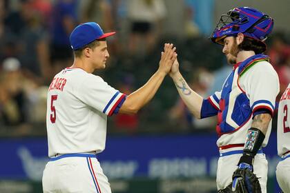 Corey Seager (izquierda) es felicitado por Jonah Heim, su compañero en los Rangers de Texas, tras la victoria ante los Marineros de Seattle, el sábado 13 de agosto de 2022 (AP Foto/LM Otero)