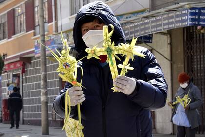 Un vendedor usa una máscara facial y guantes mientras ofrece cruces hechas de hojas de palma en un mercado de La Paz, Bolivia, durante la Semana Santa