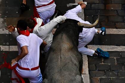 Corredores caen al suelo al paso de un toro bravo en los encierros de las Fiestas de San Fermín en Pamplona, en el norte de España, el sábado 9 de julio de 2022. (AP Foto/Álvaro Barrientos)