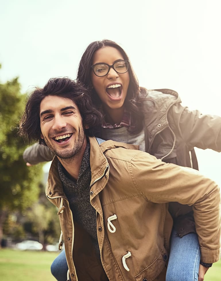 Couple, piggy back and fun for portrait in park with care, bonding and adventure in spring on holiday. Interracial love, man and woman with hug, airplane and playful on vacation with game in Toronto