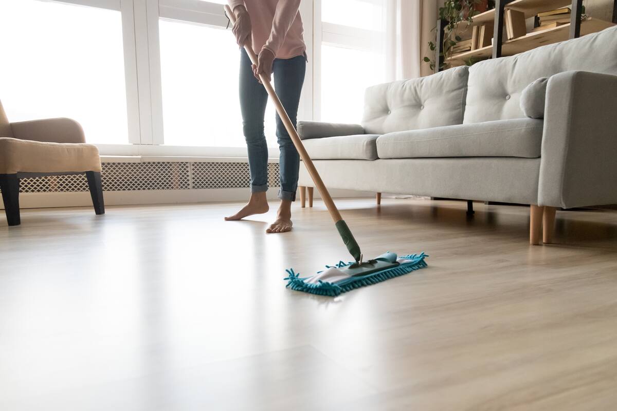 Cropped close up image of barefoot young woman in casual clothes washing heated wooden laminate warm floor using microfiber wet mop pad, doing homework cleaning routine, housekeeping job concept