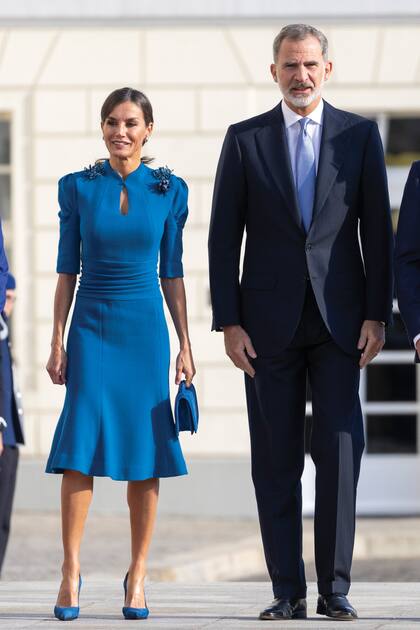 Cuando los recibieron el presidente Frank-Walter Steinmeier y la primera dama, Elke Büdenbender, Letizia vistió una creación azul de Carolina Herrera, de largo midi, vuelo bajo en la falda, manga francesa abullonada, cuello redondo y drapeado en la cintura, que acompañó con zapatos y cartera de Magrit.