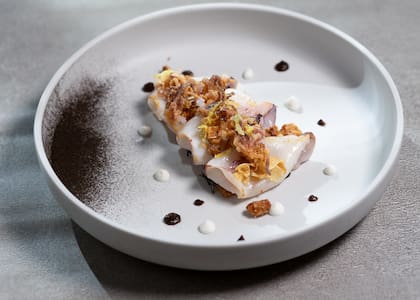 Cuerpo de chipirón a la plancha sobre un crocante de ajo, nueces y enebro, con papitas fritas y una delicada bagna cauda fría