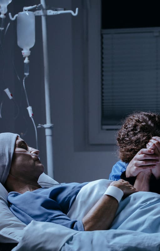 Daughter crying at her dying mother's bed in the hospital. Breast cancer concept