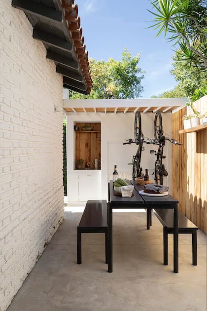 De la pérgola con perfiles de hierro y techo varillado, se cuelgan las bicis, que así no quedan expuestas a la intemperie ni ocupan espacio. La pared lindante con el vecino se revistió con tablas de madera de saligna. Mesa y bancos ‘Met’ (Estudio Te), bandeja con patas (Lapacho) y salero y pimentero (Park Design).