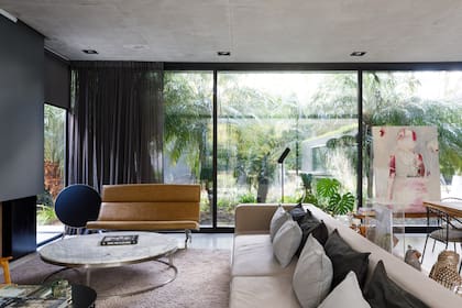 De piso a techo, los ventanales del living tienen cortinas de lino negro y, a cada lado de la chimenea, cortinas roller del mismo color.