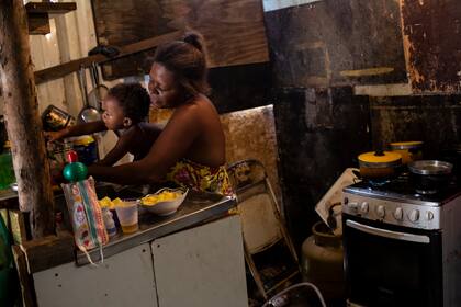 Debora Estanislau, quien antes de que empezara la pandemia de coronavirus trabajaba como empleada doméstica, sostiene a su hija de un año mientras cocina en la casa donde vive con sus cuatro hijos en la favela de Ciudad de Dios, en Río de Janeiro