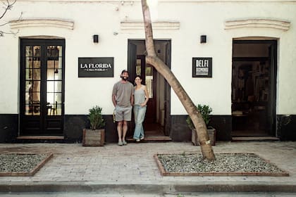 Delfina y Agustín frente a la puerta que conduce, al hotel La Florida y, al otro lado, al local deco de ella. En la vereda pusieron ladrillos sin junta por sugerencia de Flor Lagos, paisajista que también los guió con el jardín del hotel.