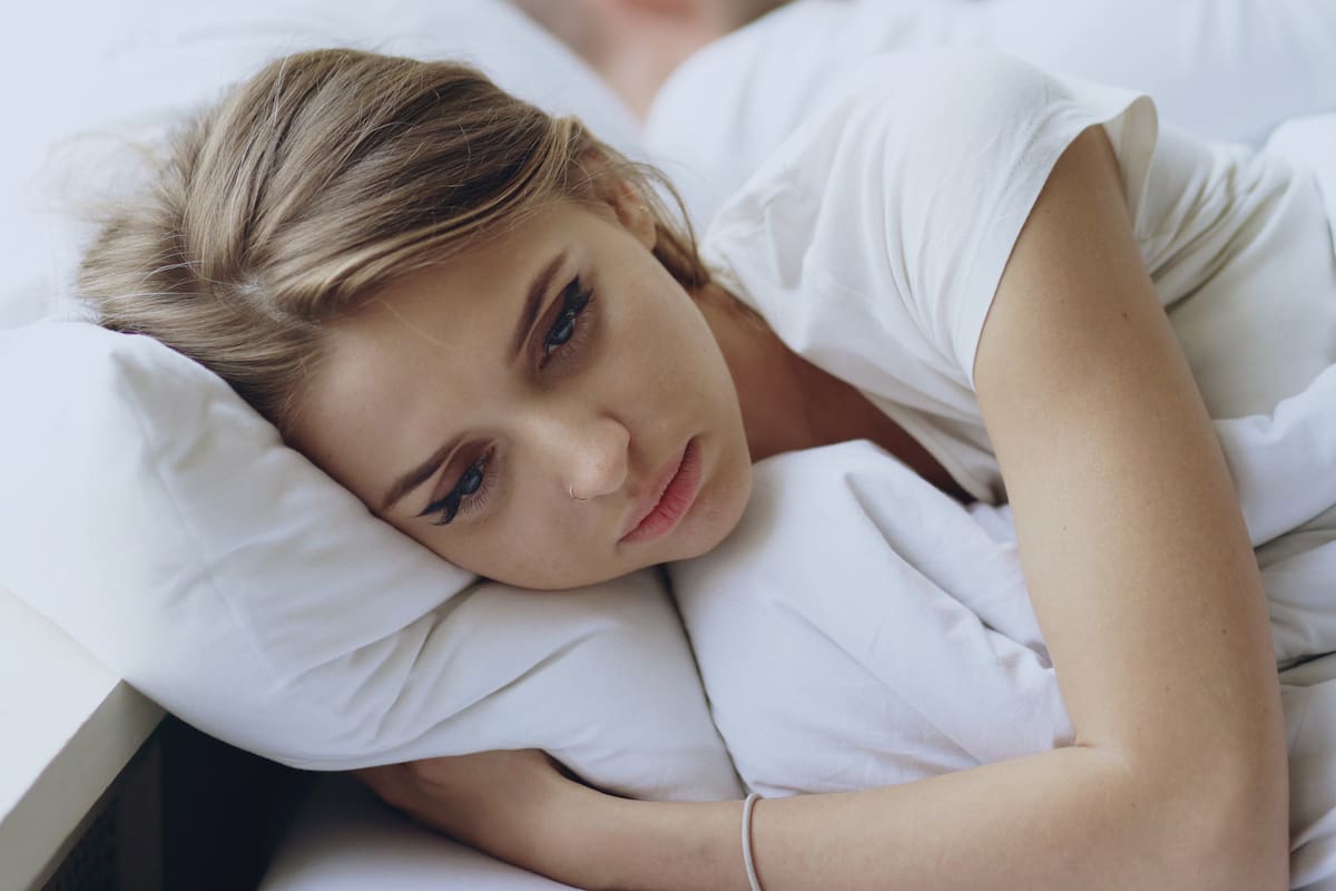 Depressed young woman lying in bed and feeeling upset after quarrel with her boylfriend in bed at home