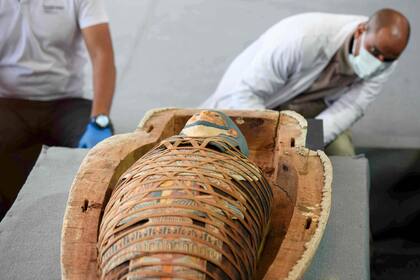 Un arqueólogo inspecciona una momia cubierta en adornos funerarios