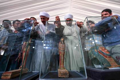 Turistas observan las estatuas y máscaras funerarias encontradas junto a los sarcófagos
