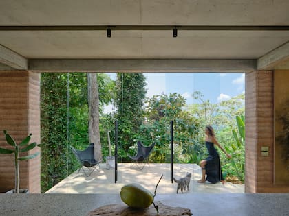 Desde el acceso, la casa se presenta como un volumen minimalista de muros de tapia, que se abre al paisaje a través de grandes paneles de vidrio corredizos.