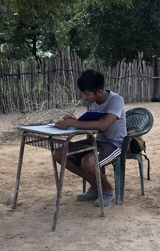 Después de volver de la escuela, Kevin saca el banco que le regalaron ahí porque no tenía escritorio a la sombra, y se pone a hacer la tarea.