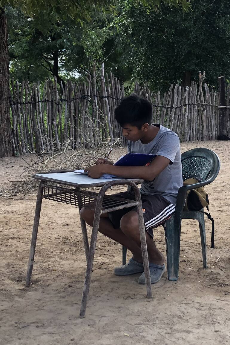 Después de volver de la escuela, Kevin saca el banco que le regalaron ahí porque no tenía escritorio a la sombra, y se pone a hacer la tarea.