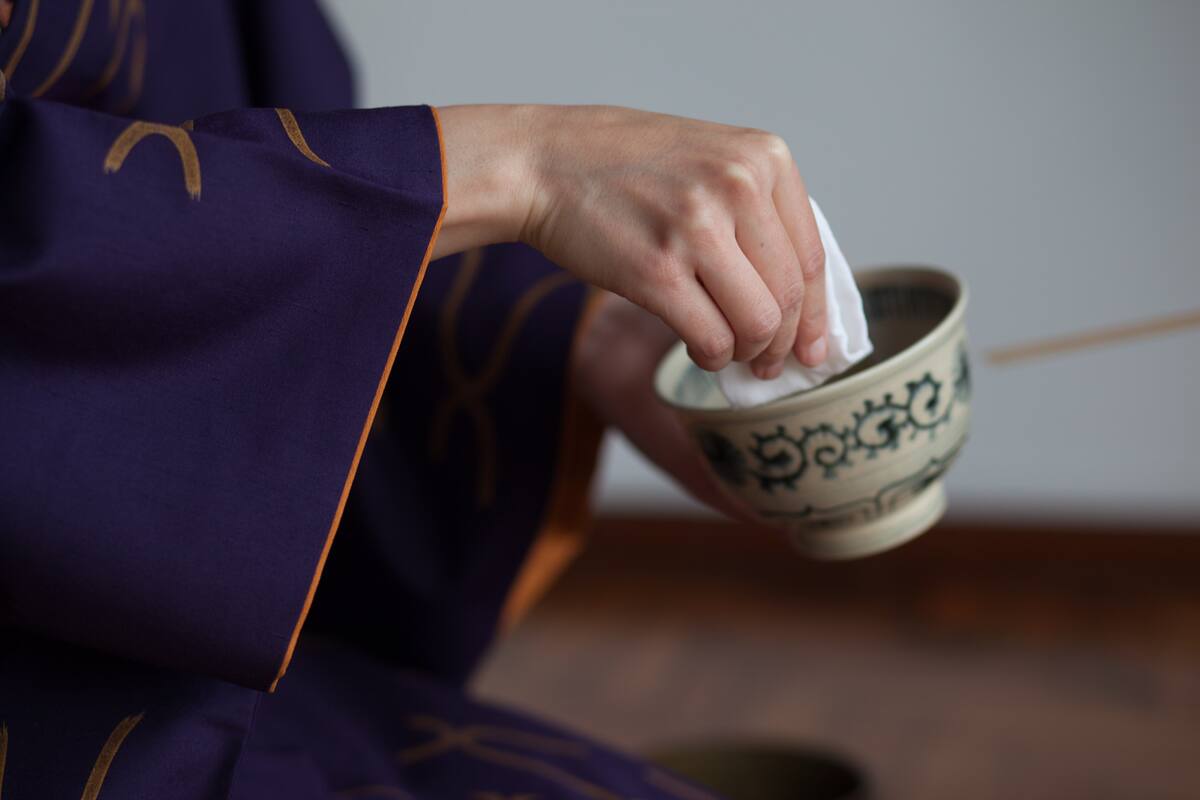 Detalle de manos limpiando cuenco en una tradicional ceremonia del té japonesa.