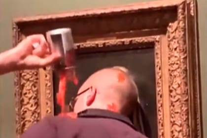 Detalle de uno de los activistas climáticos que intenta "pegar" su cabeza al cristal, que protege el cuadro de Vermeer, enchastrado con una "sustancia desconocida" que parece puré de tomate