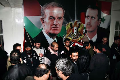 Detenidos sirios liberados se reúnen frente a carteles que muestran al presidente sirio Bashar Assad, a la derecha, y a su padre Hafez Assad tras ser liberados de la prisión de Adra, en las afueras del noreste de Damasco, Siria, el 15 de enero de 2013