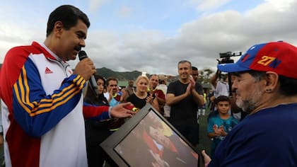Nicolás Maduro, Diego Maradona y un cuadro del ex futbolista con el ex presidente Hugo Chávez; el líder del régimen cree que el fútbol sobrepasó al béisbol como el deporte número 1 de Venezuela.