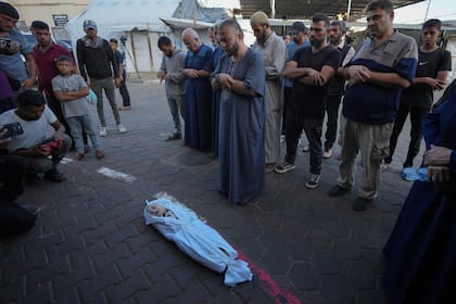 Dolientes rezan sobre el cuerpo de un niño palestino, Hosam Al Khaldi, fallecido en el bombardeo israelí sobre la Franja de Gaza, ante la morgue de un hospital en Deir al-Balah, el miércoles 9 de octubre de 2024. (AP Foto/Abdel Kareem Hana)
