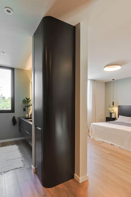 Dormitorio principal con baño en suite. Más presencia del negro en mobiliario y carpinterías, que suavizaron con textiles claros y piso vinílico simil madera (The Flooring Co).