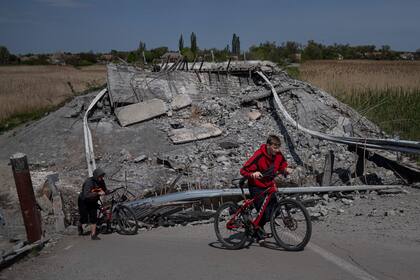 Dos adolescentes pasan en bicicleta por un puente destruido cerca de Orihiv, Ucrania, el 5 de mayo de 2022. (AP Foto/Evgeniy Maloletka)