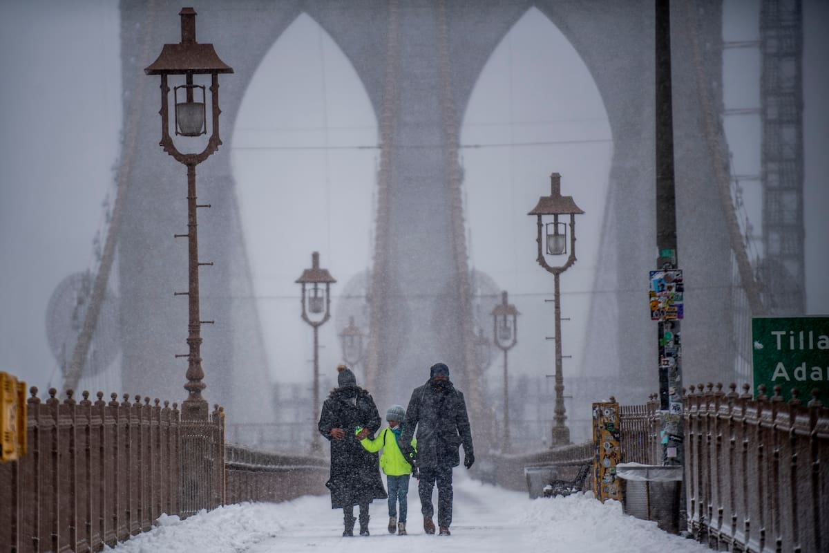 Dos adultos y un niño cruzan el puente de Brooklyn durante una tormenta de nieve.