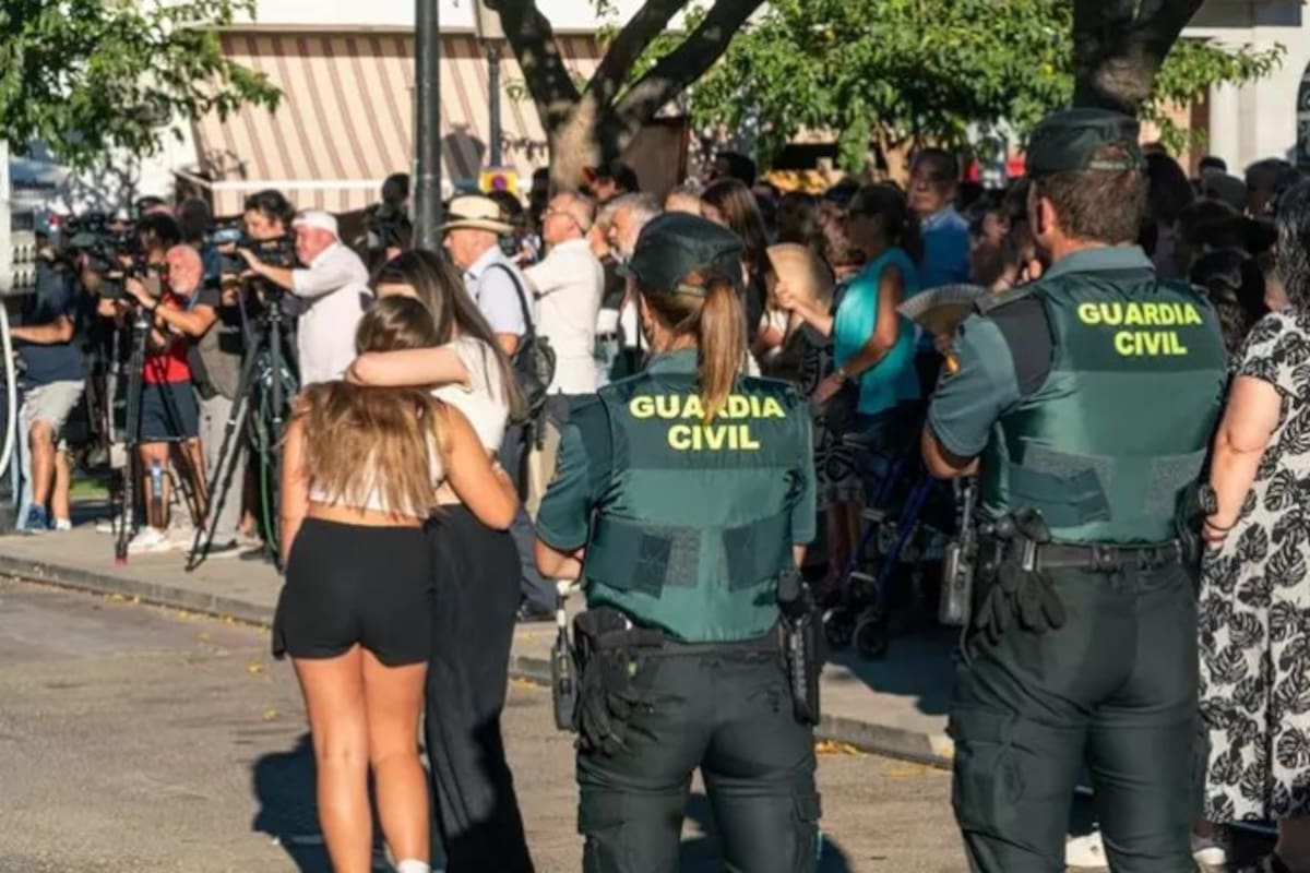 Dos agentes de la Guardia Civil observan a dos chicas abrazadas durante el minuto de silencio por el asesinato de un menor, en la puerta del Ayuntamiento de Mocejón (Europa Press)
