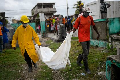 Dos hombres cargan con el cuerpo de un niño, hallado entre los escombros de un edificio derruido, hasta el cementerio de Les Cayes, Haitó, el 17 de agosto de 2021, tres días después de un sismo de magnitud 7,2 que remeció la parte suroccidental del país. (AP Foto/Matías Delacroix)