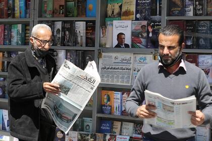 Dos hombres leen periódicos locales con titulares sobre los últimos eventos en su país, frente a un quiosco en la capital