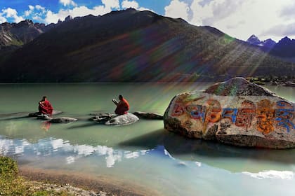 Dos monjes tibetanos en las orillas del lago Yilung Lhatso en el este del Tíbet. El grabado en la roca dice Om Mani Padme Hum, que es el mantra del Buda de la Compasión