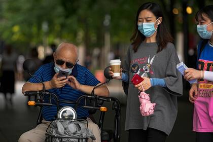 Dos mujeres con mascarillas para protegerse del coronavirus pasan junto a un hombre que revisa su celular, el martes 20 de julio de 2021, en Beijing. (AP Foto/Andy Wong)