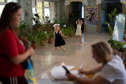 Dos niñas juegan mientras una mujer distribuye pastillas de yodo, por si se produce una fuga de radiación en la central nuclear de Zaporiyia, en una escuela, en Zaporiyia, Ucrania, el 2 de septiembre de 2022. (AP Foto/Leo Correa)