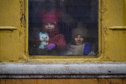 Dos niños miran por la ventana de un tren sin calefacción que se dirige a Leópolis, en Kiev, Ucrania