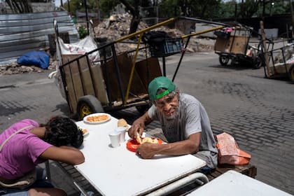 Dos personas almorzando una comida gratuita del comedor social de la Casa Comunitaria del Fondo, en el barrio Padre Carlos Múgica de Buenos Aires, Argentina, el jueves 14 de diciembre de 2023. (AP Foto/Rodrigo Abd)