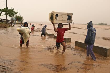 Dos personas cargan sus pertenencias junto a un río crecido tras intensas lluvias causadas por el tifón Toraji, el lunes 11 de noviembre de 2024, en Ciudad Ilagan, provincia de Isabela, en el norte de Filipinas. (AP Foto/Noel Celis)
