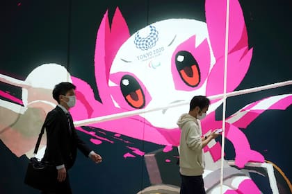 Dos personas, con mascarilla para protegerse del coronavirus, pasan junto a un anuncio de los Juegos Paralímpicos de Tokio 2020, en Tokio, el 14 de mayo de 2021. (AP Foto/Eugene Hoshiko)