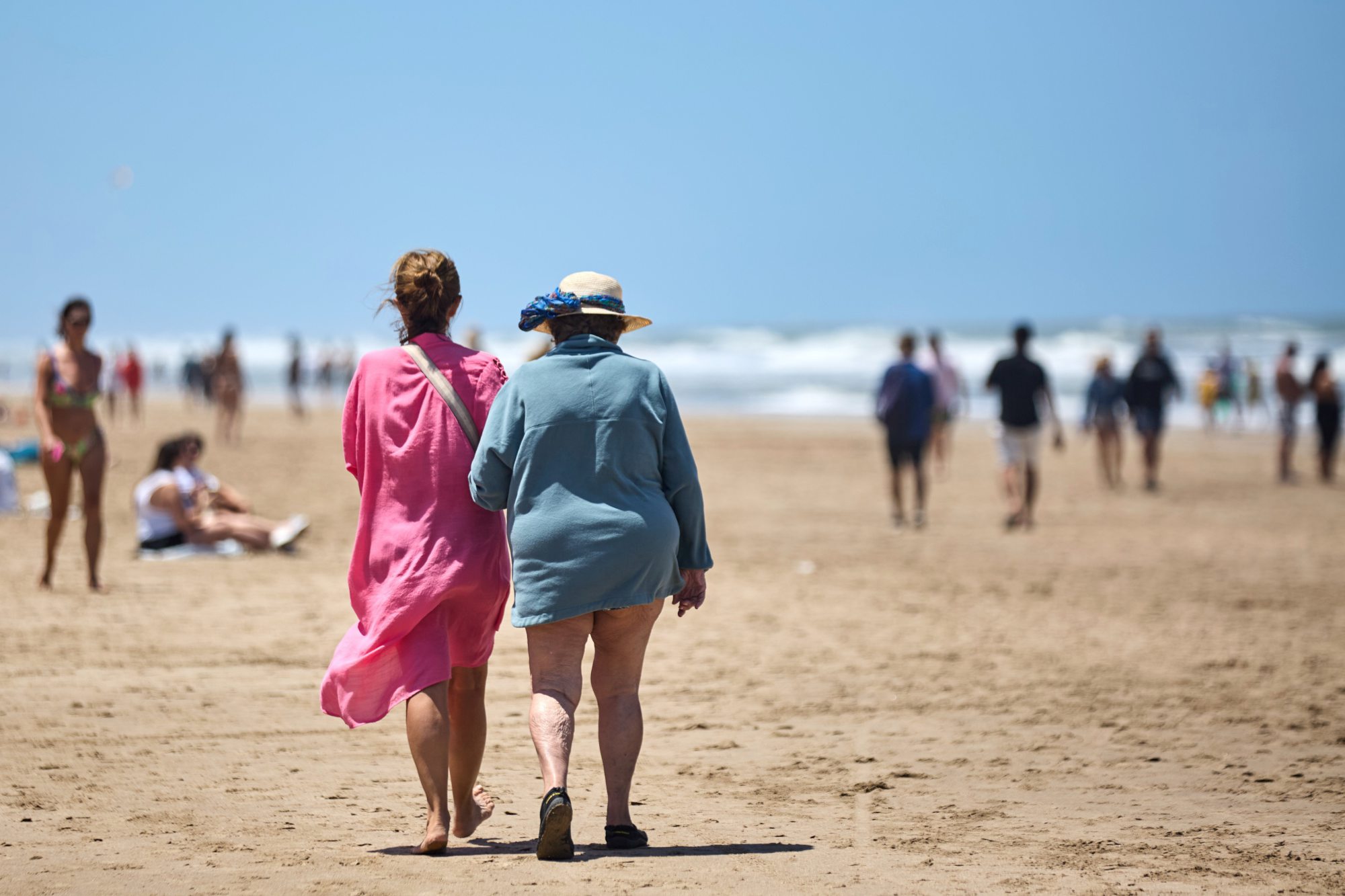 Dos personas mayores caminan por la orilla en Pinamar, en una escena cotidiana que se repite cada verano