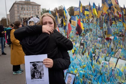 Dos personas se abrazan durante un minuto de silencio en memoria de los soldados caídos en la defensa del país durante la guerra en Rusia, en el Día de los Defensores, en un memorial improvisado en la Plaza de la Independencia de Kiev, Ucrania, el 1 de octubre de 2024. (AP Foto/Efrem Lukatsky)