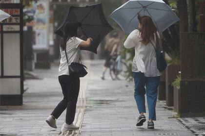 Dos personas tratan de mantener sus paraguas abiertos ante los fuertes vientos de un tifón que se acerca a Kagoshima, al oeste de Japón, el 29 de agosto de 2024, (Hidetaka Komukai/Kyodo News vía AP)