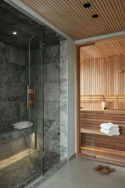 Dos propuestas bien marcadas: hacia la derecha, el sauna seco, con revestimiento en madera; hacia la izquierda, el sauna húmedo, en mármol gris.