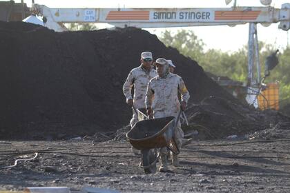 Dos soldados mexicanos empujan carretillas en las labores de rescate de 10 mineros atrapados en una mina de carbón inundada, el jueves 4 de agosto de 2022, en Sabinas, estado de Coahuila, México. (AP Foto/Alfredo Lara)