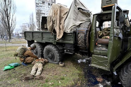 Un médico militar ucraniano (izq.) examina el cuerpo de una persona que yace junto a un vehículo después de que él y los miembros de un grupo de asalto recibieron disparos durante un enfrentamiento en la capital ucraniana de Kiev.