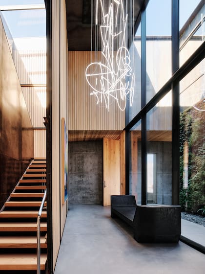 El acceso se revela como un pasaje de luz y naturaleza: un pasillo enmarcado por muros de vidrio y un jardín vertical que anticipa la serenidad interior.